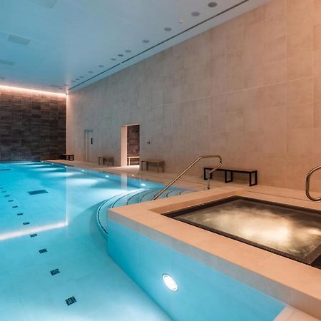 Citysuites 2 Aparthotel Salford  Esterno foto The photo shows an indoor swimming pool area. The pool is a bright blue color and features smooth, tiled surfaces. On one side, there is a hot tub area with steps leading into it. The walls are made of light-colored stone, and there is ambient lighti