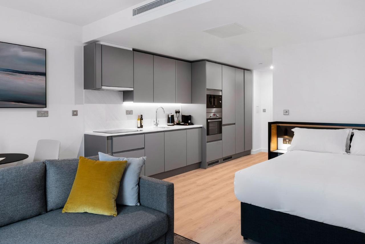 Citysuites 2 Aparthotel Salford  Esterno foto The photo shows a modern studio apartment featuring an open-plan layout. On one side, there is a kitchenette with sleek, gray cabinets and appliances, including a coffee maker and oven. Adjacent to the kitchenette is a small dining area with a table 