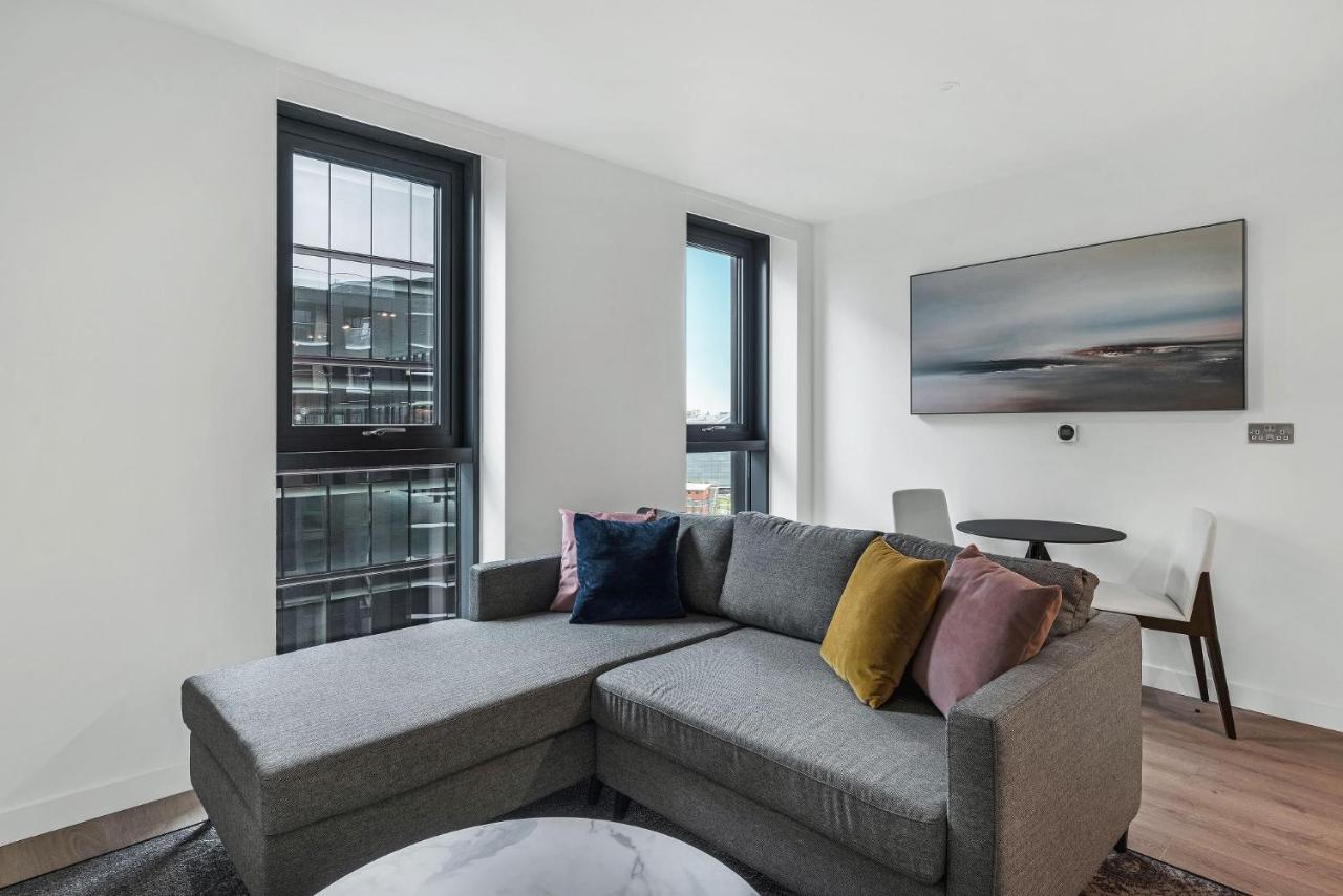Citysuites 2 Aparthotel Manchester Esterno foto The photo shows a modern living space featuring a gray sectional sofa adorned with colorful throw pillows. There are large windows allowing natural light to fill the room, offering a view of the outdoors. A wall-mounted television is positioned above