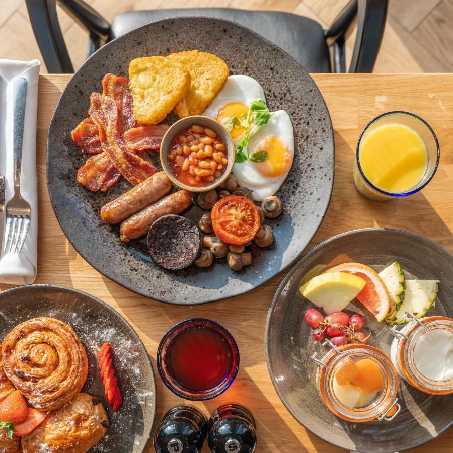 Citysuites 2 Aparthotel Manchester Esterno foto The photo showcases a delicious breakfast spread. On a large, dark plate, there are items including crispy bacon, two fried eggs, baked beans, a grilled tomato, sautéed mushrooms, sausage links, and slices of black pudding. There's also a few pieces 