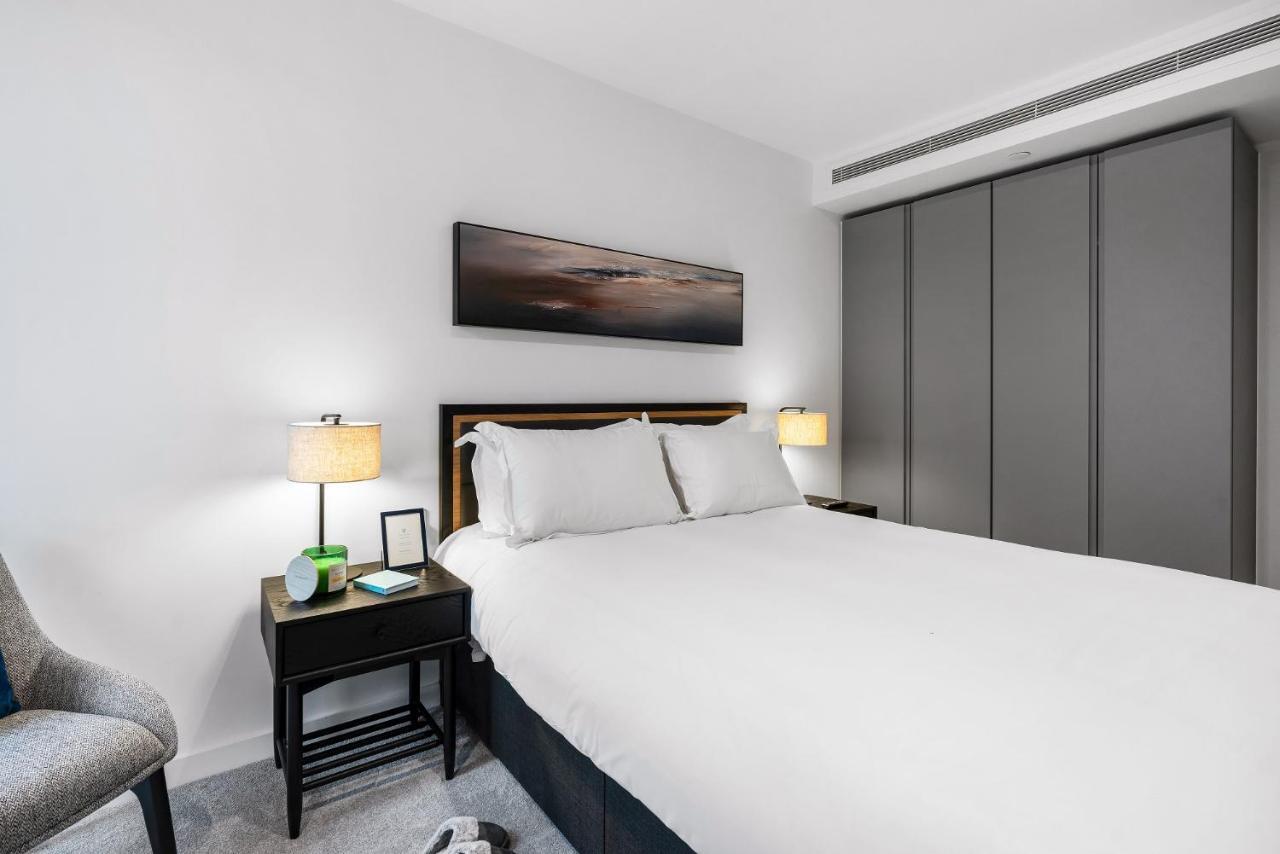 Citysuites 2 Aparthotel Manchester Esterno foto The photo shows a modern bedroom with a neatly made bed featuring white linens and pillows. Flanking the bed are two bedside tables, each with a lamp providing soft lighting. There is a piece of artwork above the bed, which appears to depict a landsc