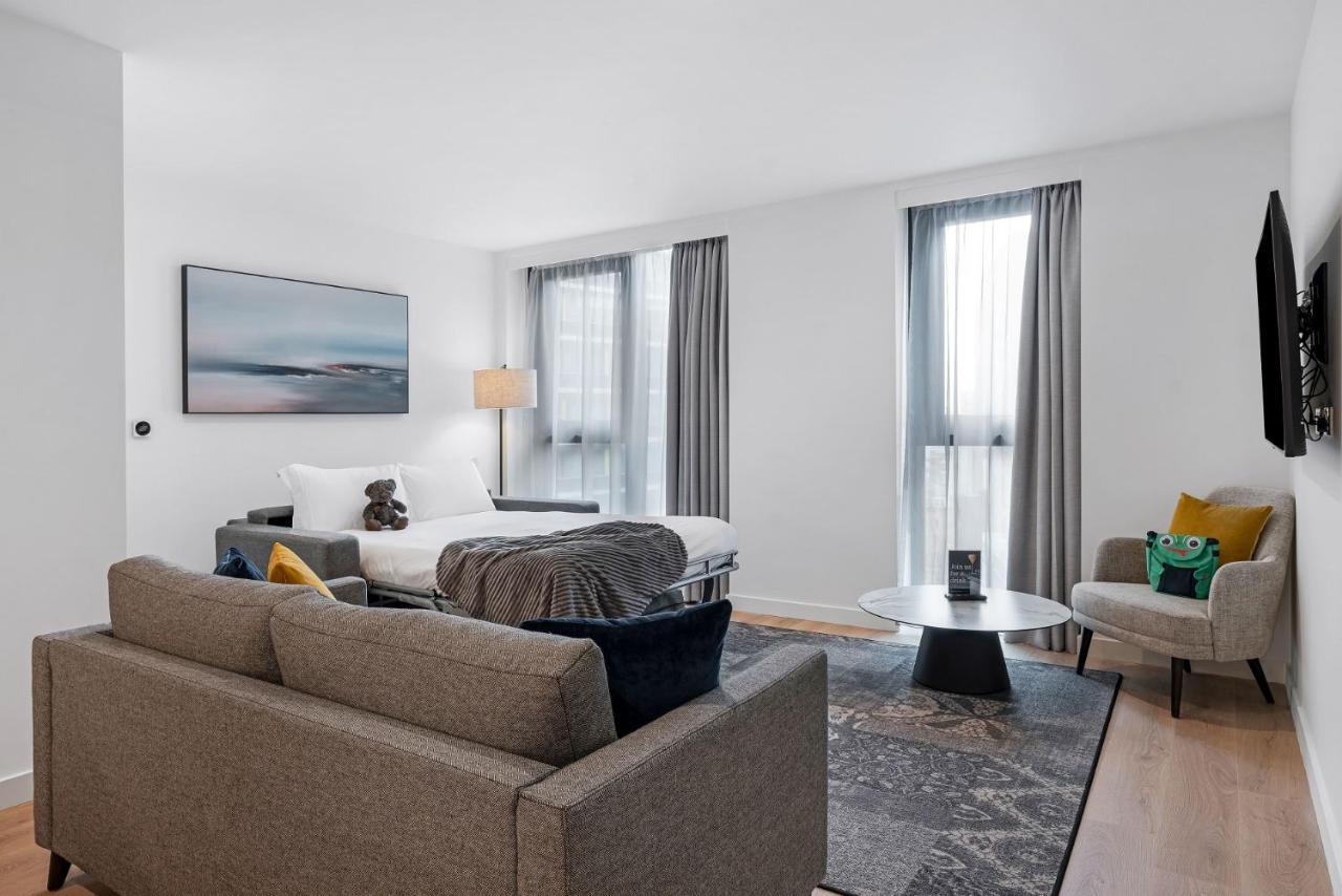 Citysuites 2 Aparthotel Manchester Esterno foto The photo shows a modern living space that incorporates a cozy and inviting atmosphere. It features a light-colored couch with colorful cushions, positioned in front of a coffee table. There's a comfortable armchair nearby, and a throw blanket is dra