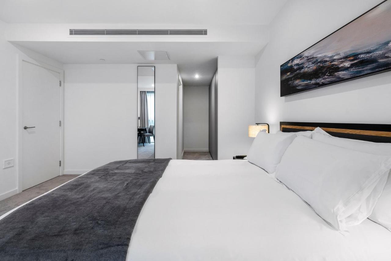 Citysuites 2 Aparthotel Manchester Esterno foto The photo shows a modern bedroom with a minimalistic design. In the foreground, there is a neatly made bed with white linens and a dark gray throw blanket. To the side, there is a bedside lamp and a piece of abstract artwork on the wall above the bed