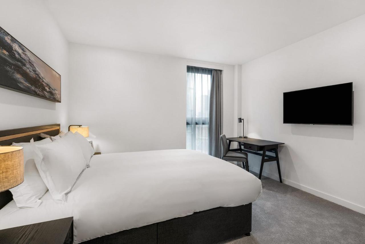 Citysuites 2 Aparthotel Manchester Esterno foto The photo shows a modern hotel room featuring a large bed with white linens and a dark headboard. There are two bedside lamps on either side of the bed. A desk with a chair is placed against one wall, and a flat-screen TV is mounted on another wall. 