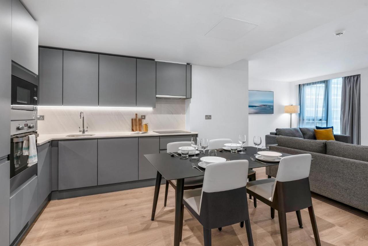 Citysuites 2 Aparthotel Salford  Esterno foto The photo shows a modern, open-concept kitchen and living area. The kitchen features sleek, gray cabinetry with a countertop, a sink, and built-in appliances. There are cooking utensils displayed on the countertop. Next to the kitchen, there is a din