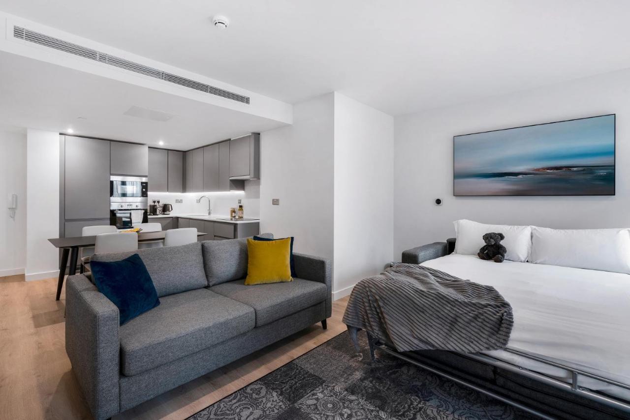 Citysuites 2 Aparthotel Manchester Esterno foto The photo shows a modern, open-concept living space that includes a kitchen and a sleeping area. 

- **Living Area**: On the left, there's a gray sofa with a blue and yellow throw pillow. A blanket is draped over one side, and there's a small dark ru