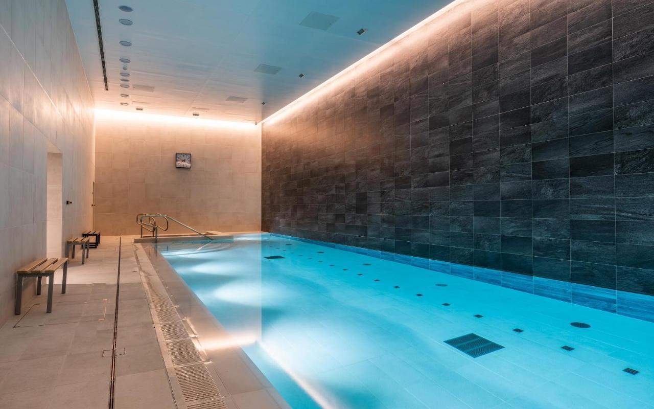 Citysuites 2 Aparthotel Manchester Esterno foto The photo shows an indoor swimming pool area. The pool is illuminated with a soft blue light, creating a calming atmosphere. The walls are designed with dark tiles, and there is a lighter tiled area surrounding the pool. Ambient lighting is installed