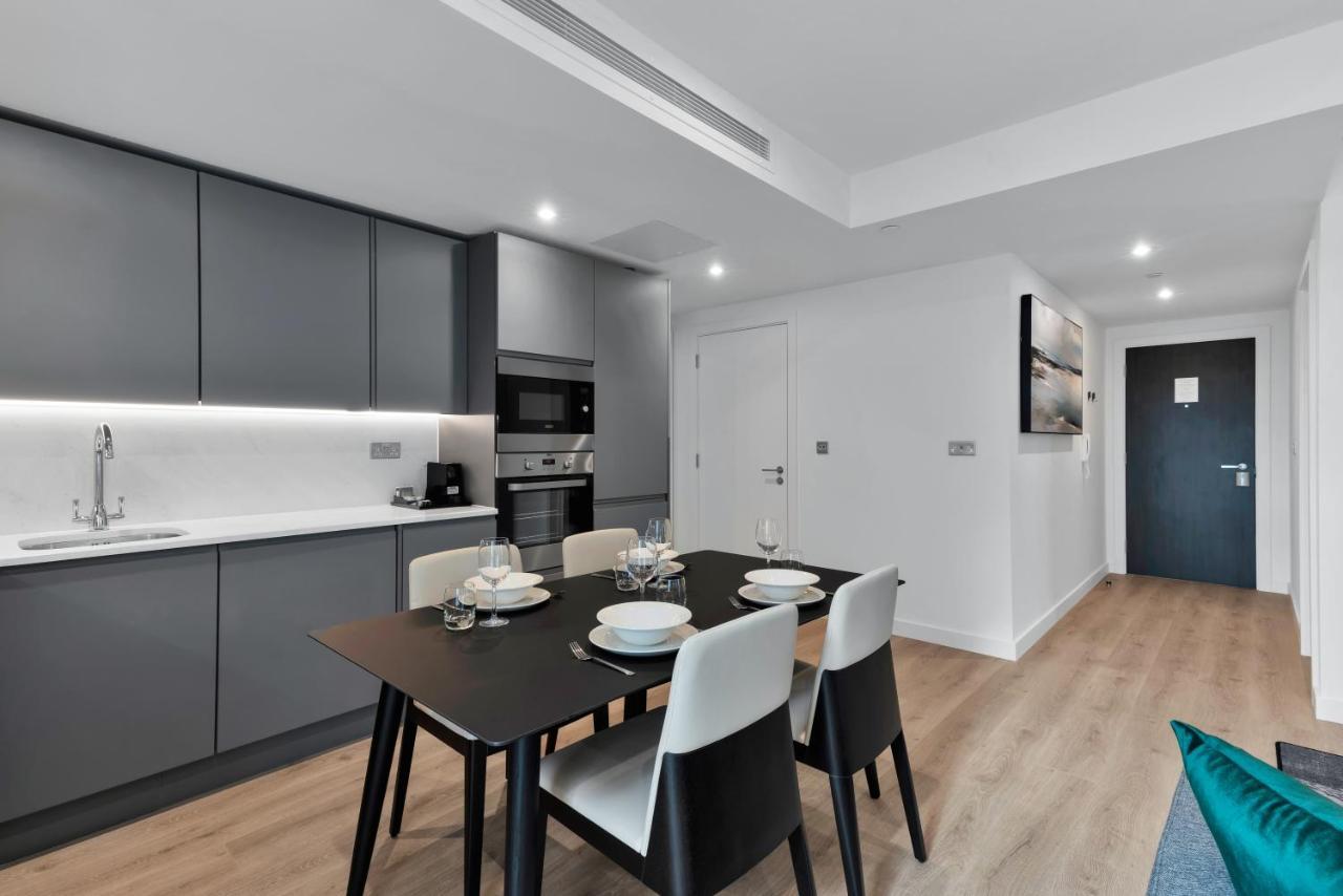 Citysuites 2 Aparthotel Manchester Esterno foto The image shows a modern kitchen and dining area. The kitchen features sleek gray cabinets with a white countertop, and it is equipped with appliances such as a microwave. There’s a dining table set for four, with white plates and glasses ready. The 