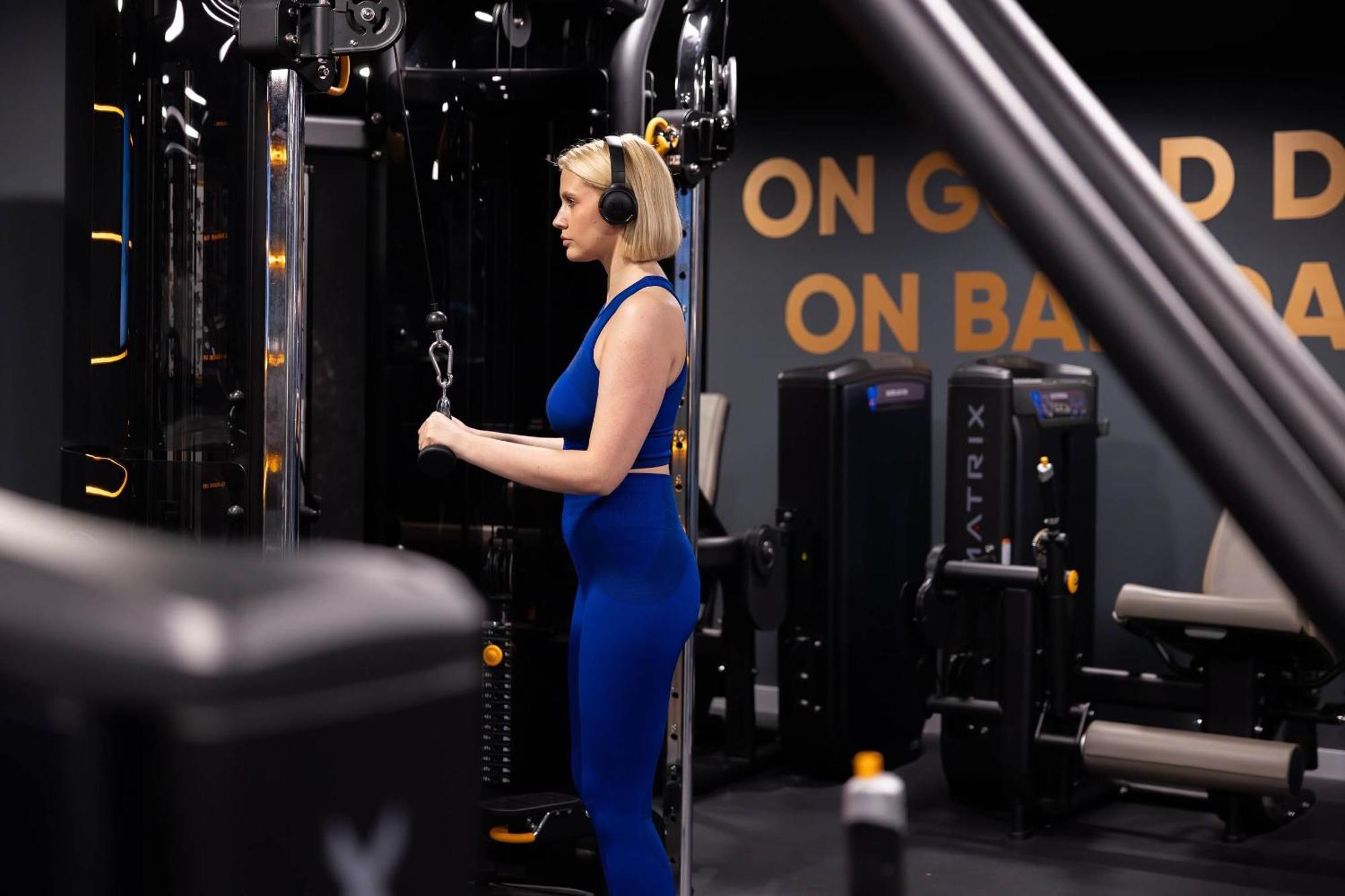 Citysuites 2 Aparthotel Manchester Esterno foto The photo shows a woman working out in a gym. She is wearing a blue athletic outfit and headphones while using a gym machine. The background features various other gym equipment and a wall with the words "ON GOOD ON BAD" displayed prominently. The se