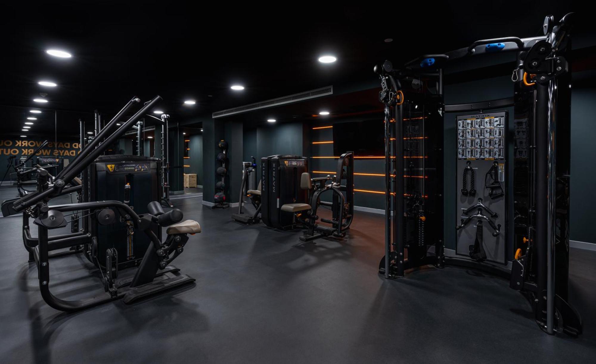 Citysuites 2 Aparthotel Manchester Esterno foto The photo shows a modern gym or fitness area with various workout machines. The space has a dark color scheme, featuring black walls and flooring. There are multiple pieces of exercise equipment, including stations for strength training, possibly tar