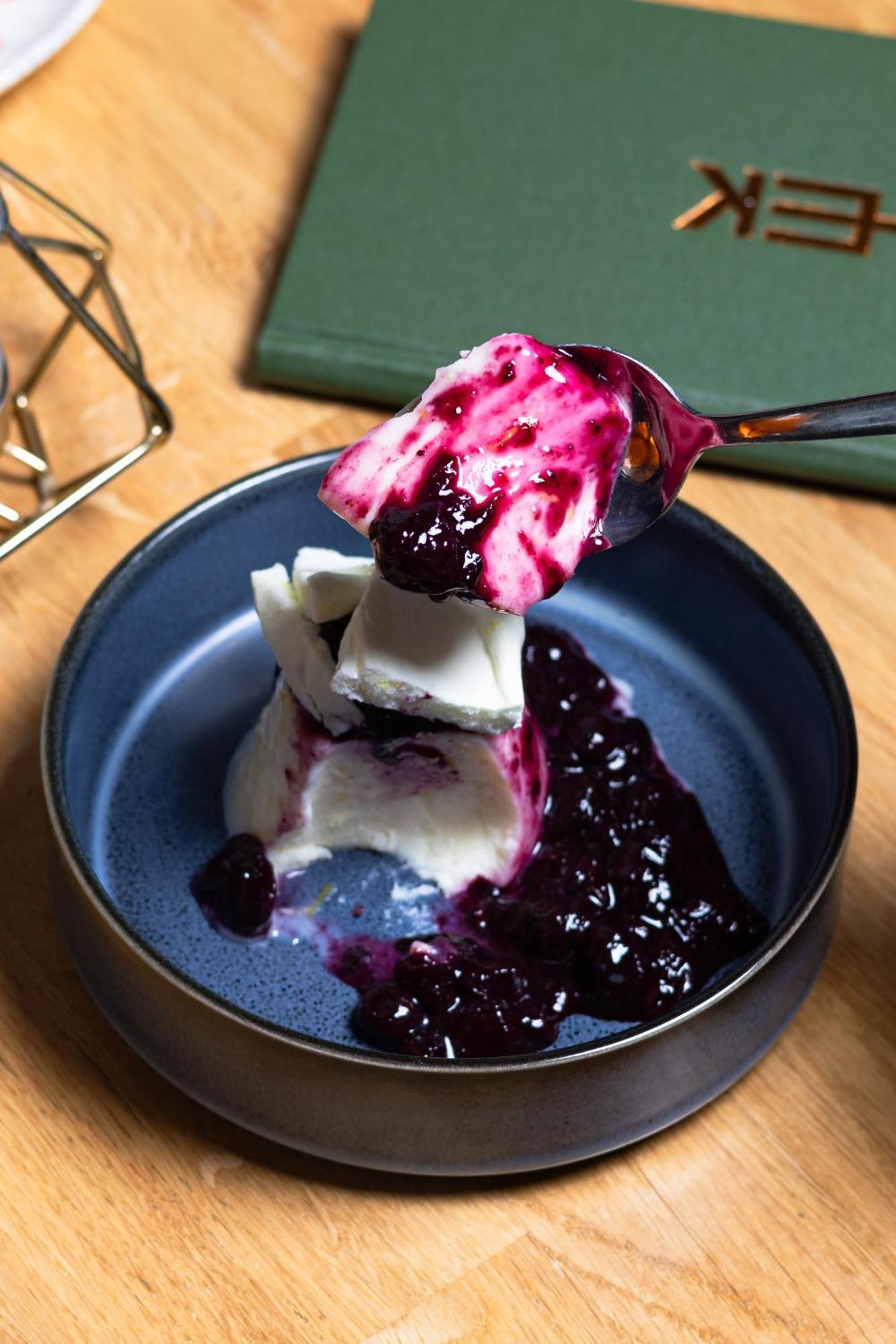 Citysuites 2 Aparthotel Manchester Esterno foto The photo shows a serving of dessert, likely a type of panna cotta or a creamy custard, partially dished out and accompanied by a rich berry sauce, possibly made from blueberries or blackberries. A spoon with some of the dessert and sauce is hovering